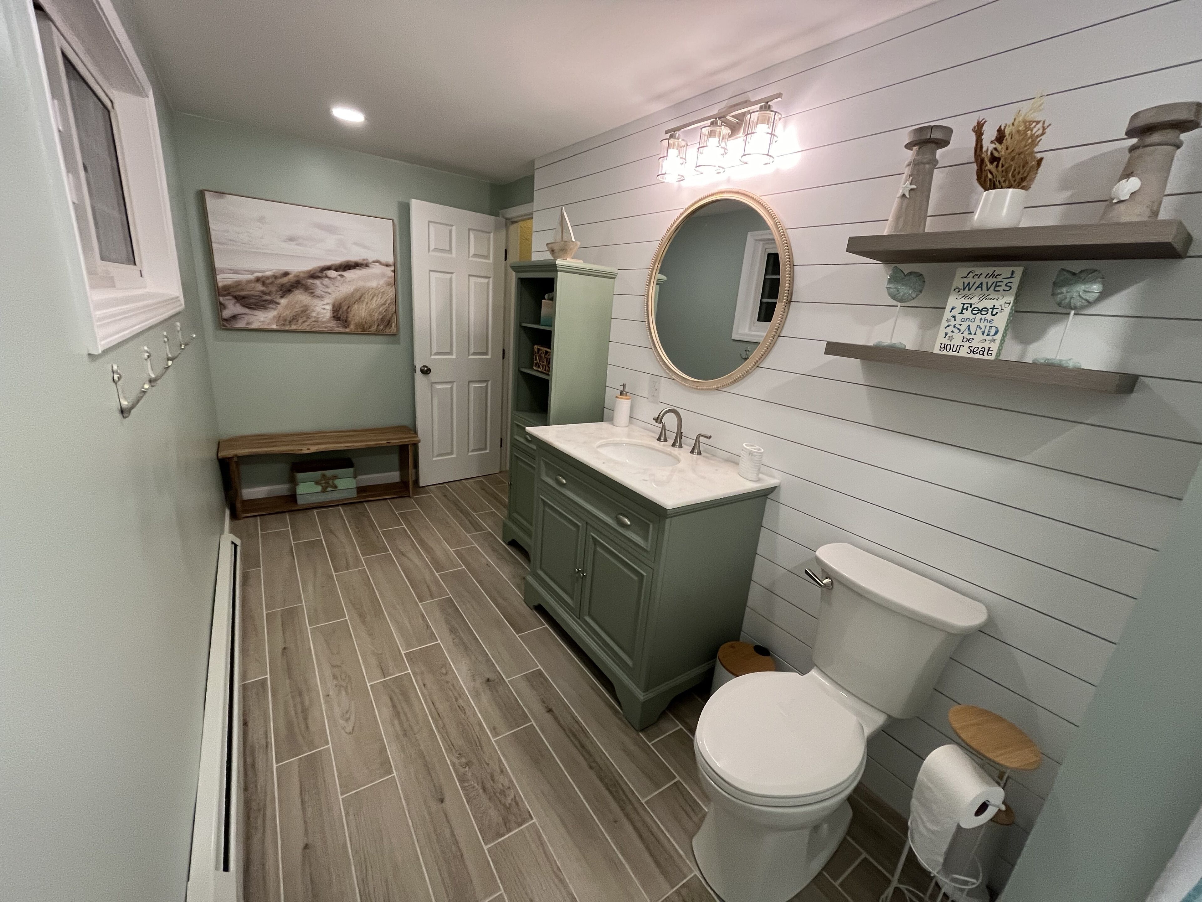 A bathroom with a sink, mirror, toilet, and a bench.