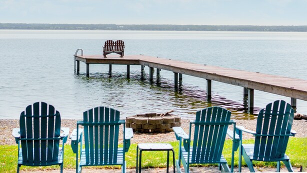 Uitzicht op een meer met een houten steiger die in het water uitloopt, met twee Adirondack-stoelen en een klein tafeltje.