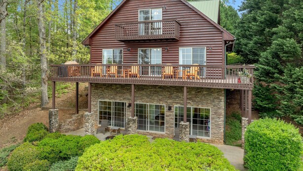 A two-story log cabin with a balcony, stone foundation, and a view of the surrounding forest. - Log Cabin On Lake Keowee-Big Lake Mountain Views (Six Mile)