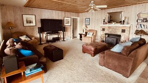 A cozy living room with a fireplace, leather sofas, a television, and a ceiling fan.