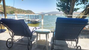 Two outdoor lounge chairs with wheels, a small round table, and a view of a lake with boats and hills in the background.