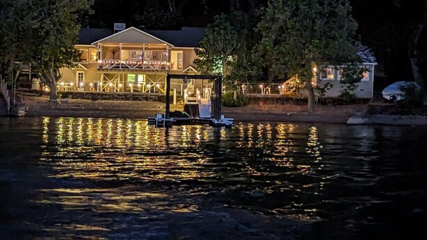 A waterfront property with a large house featuring a covered deck and a boat dock.