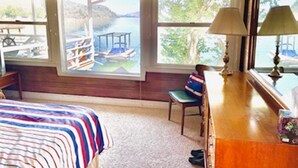 A room with a bed, a desk, a chair, and large windows overlooking a body of water.