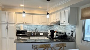 A modern kitchen with white cabinets, a granite countertop, a built-in microwave, and a coffee maker. There is a wooden dining table with chairs and a window with a view.