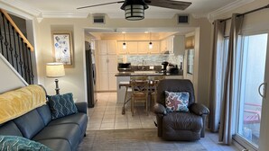 A modern living room with a sofa, a leather chair, and a dining area with a kitchen in the background.