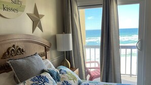 A bedroom with a bed, a star decoration, a nightstand, a lamp, and a view of the ocean through a window.