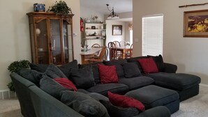 Ein Wohnzimmer mit Ecksofa, einer Holzkassette, einem Esstisch mit Stühlen und einem Bild an der Wand.