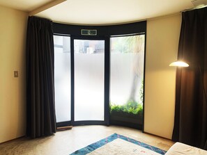 A hotel room with a large sliding door leading to a balcony, a small rug on the floor, and a wall-mounted light fixture. - A Designer Space In Central Kyoto (Nakagyoku)