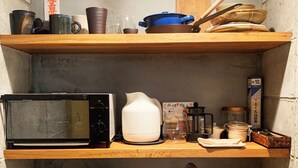 Et lille køkken med mikroovn, kaffemaskine og vask. Træhylder over vasken med forskellige køkkenartikler.