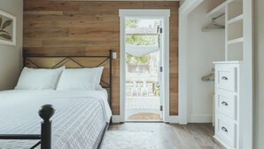 A bedroom with a wooden wall, a bed with white bedding, a white dresser, and a door leading to an outdoor patio. - Contemporary Boutique Bungalow+Backyard+Walkable (San Luis Obispo)
