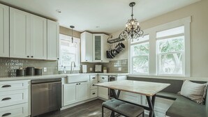 A modern kitchen with white cabinetry, a built-in dishwasher, a dining table with a bench, and a chandelier. - Contemporary Boutique Bungalow+Backyard+Walkable (San Luis Obispo)