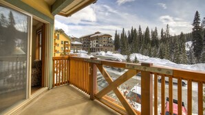 A wooden balcony with a view of a snow-covered landscape and buildings. - Convenient and located in the resort village (Sun Peaks)