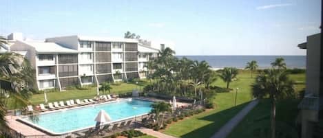 A hotel with a swimming pool, palm trees, and a view of the ocean.
