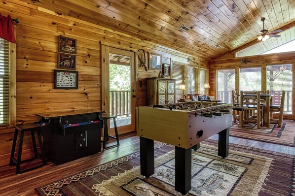 A cozy room with wooden walls, a foosball table, and a pool table.