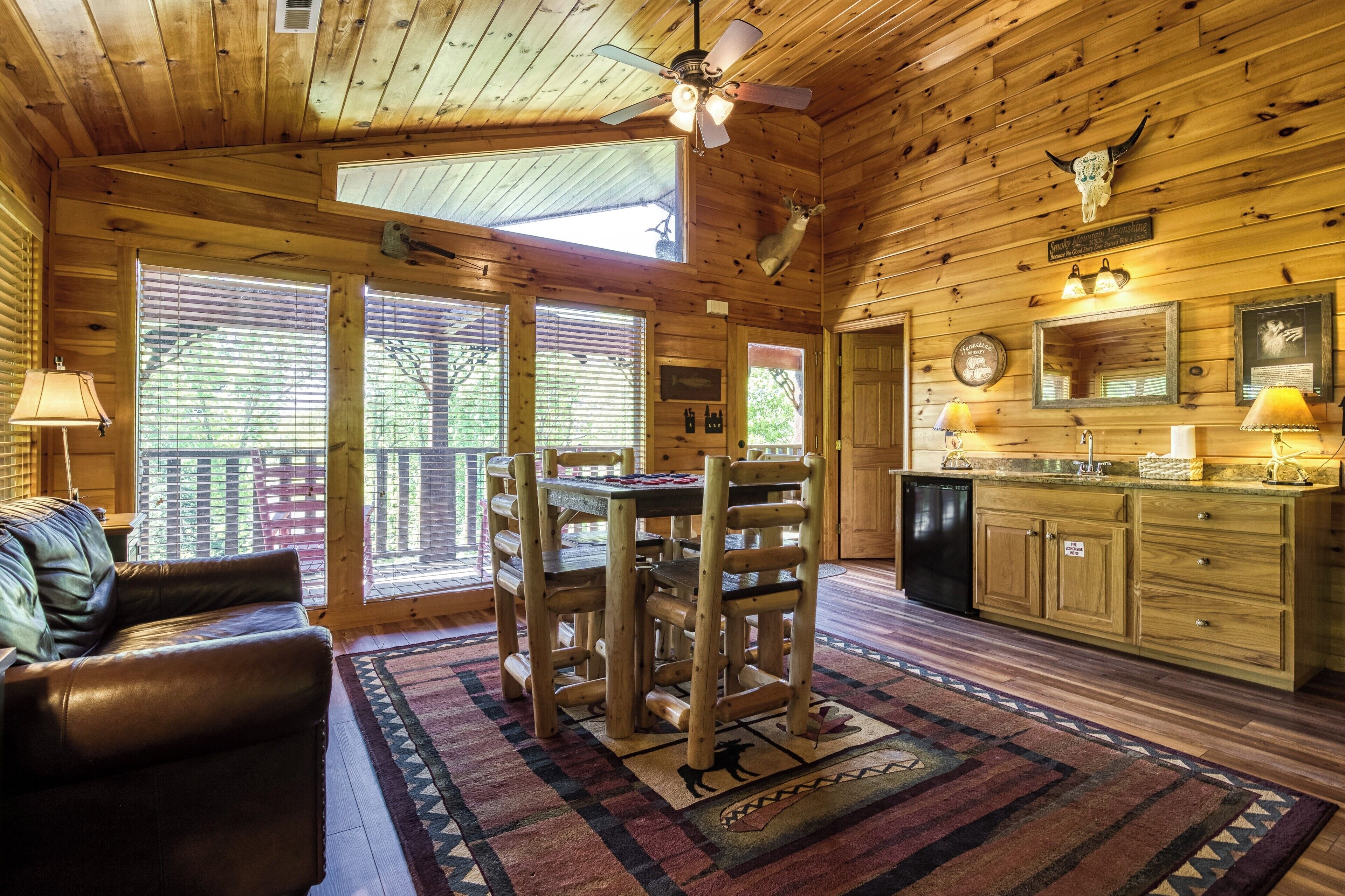 Interior de una cabaña de madera con una mesa de comedor, sillas, un sofá y una zona de cocina.