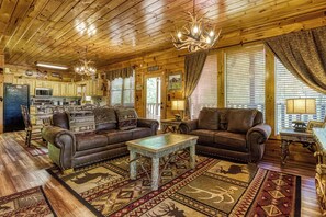 L’intérieur chaleureux d’un chalet avec un plancher en bois, des canapés en cuir, une table à manger et un lustre.