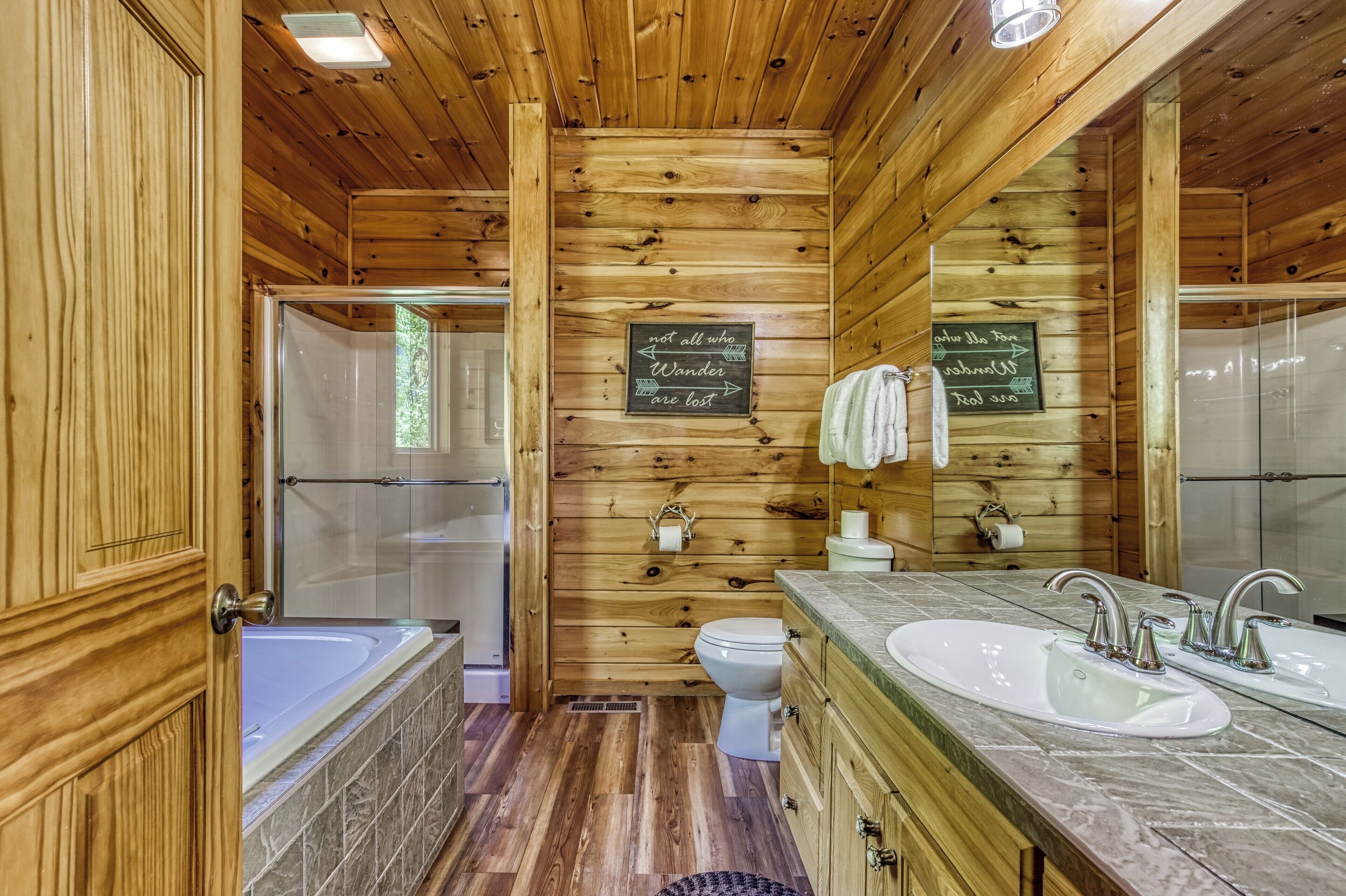 Ein Badezimmer einer Holzhütte mit Badewanne, Toilette und einem großen Spiegel.