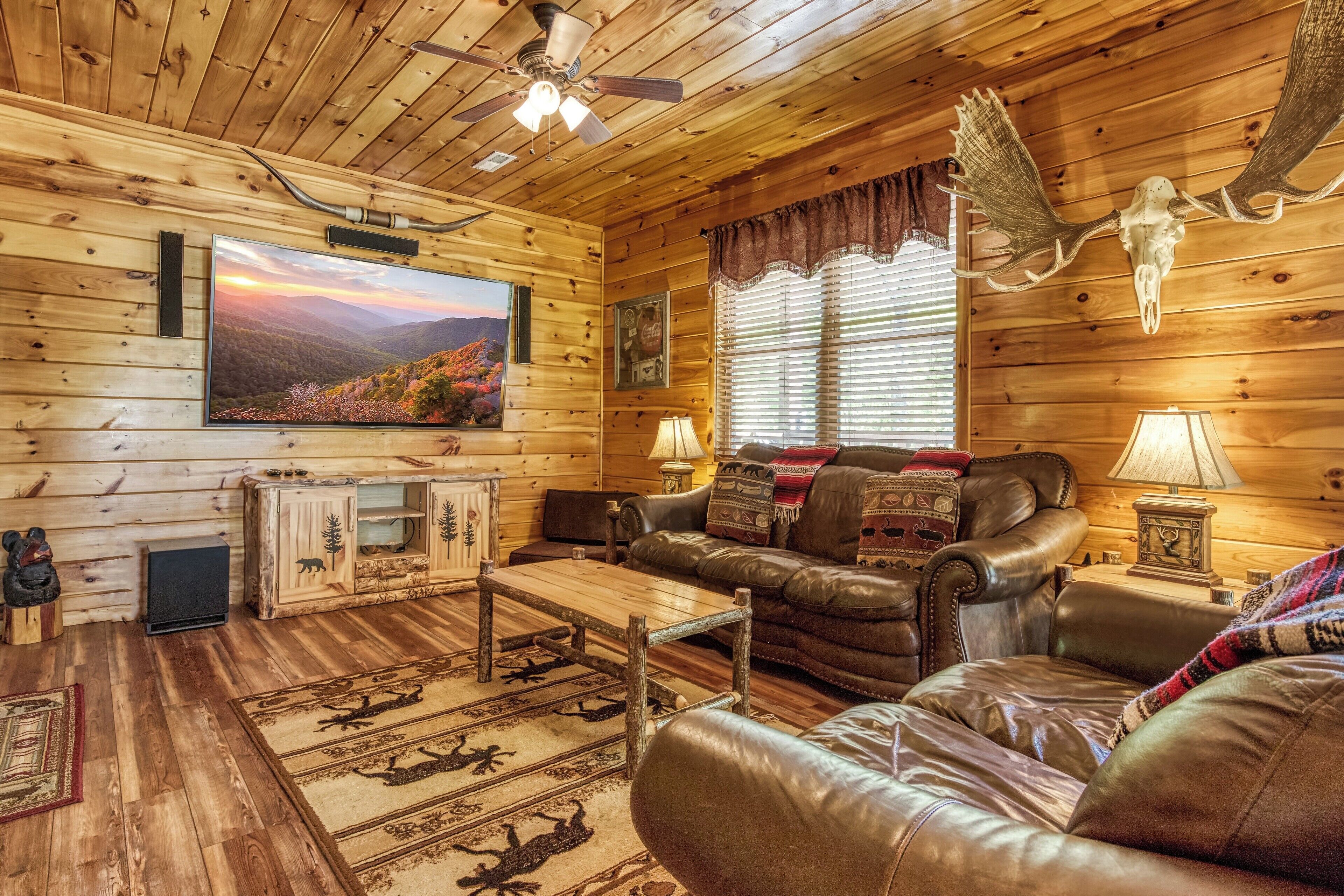 Een gezellig chaletinterieur met houten wanden, een leren bank, een houten salontafel en een tv met een prachtig landschap.