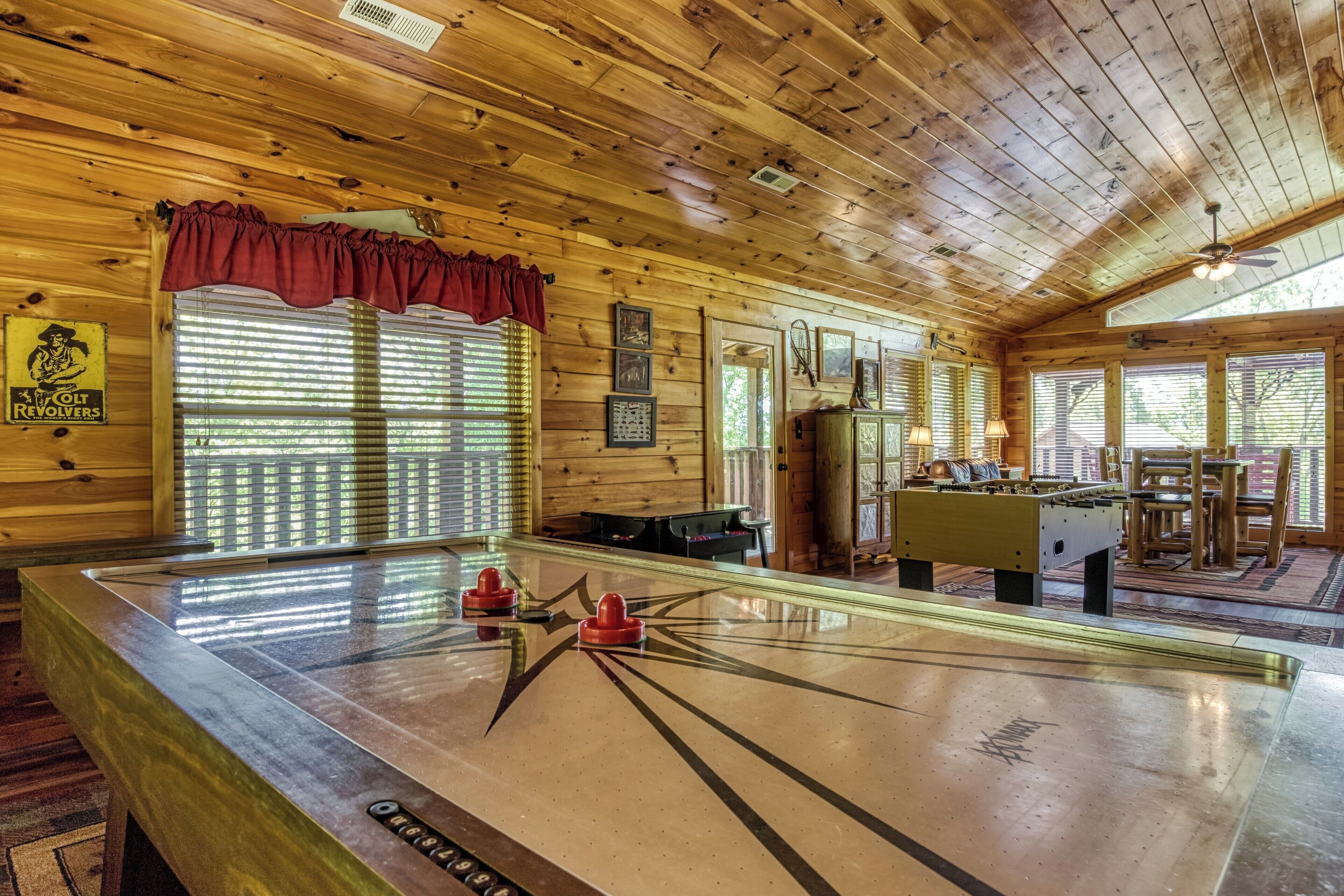 A wooden-floored room with a foosball table, a billiards table, and a billiard cue rack.