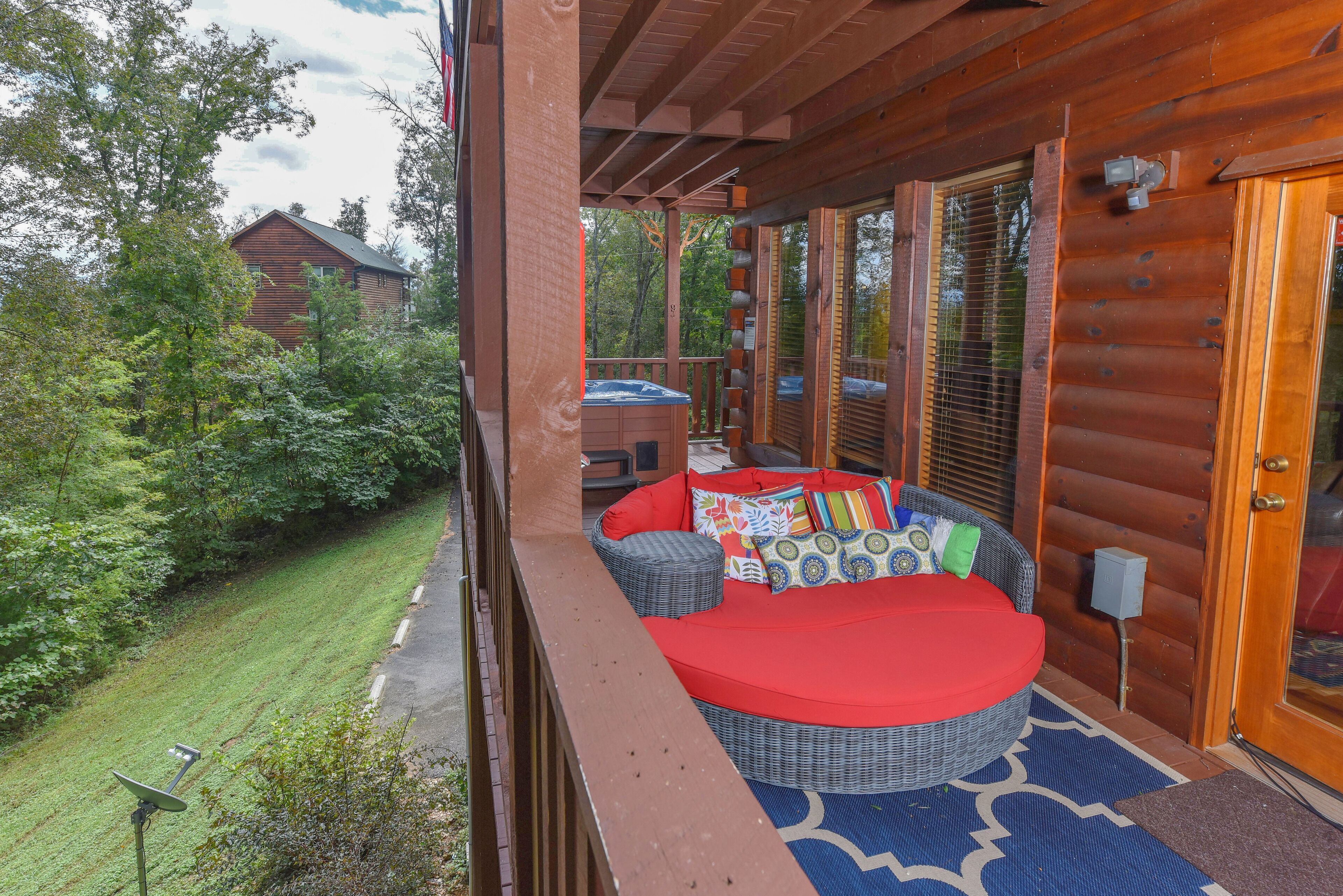 Une cabane en rondins dotée d’un balcon avec un canapé en osier et des coussins rouges, ainsi qu’un bain à remous.
