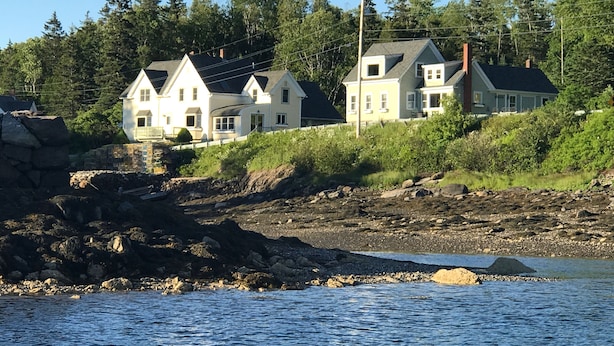 Une propriété située sur la côte, comprenant deux maisons, un rivage rocheux et une vue dégagée sur l’eau.