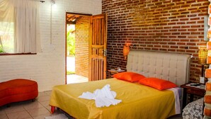 Une pièce avec un lit, une chaise rouge, une porte en bois et un mur en briques.
