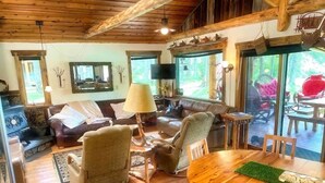 A cozy cabin interior with a wooden dining table, leather sofas, and a fireplace. - Swan River Retreat: 5 Cabins on River. Sleeps 30.  Family Reunions! (Bigfork)