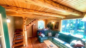 A wooden interior with a staircase, a green sofa, and a view of the outdoors. - Swan River Retreat: 5 Cabins on River. Sleeps 30.  Family Reunions! (Bigfork)