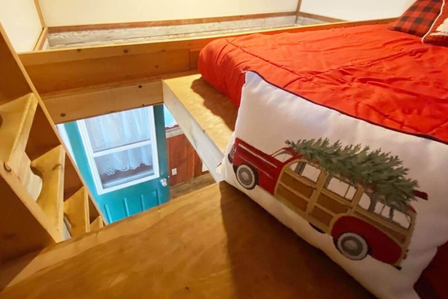 Une chambre avec un lit en mezzanine, une fenêtre et un coussin rouge et blanc orné d’un motif représentant une voiture et un sapin de Noël.