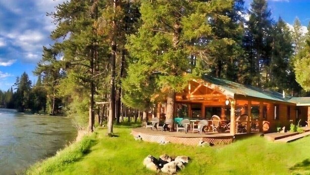 A cabin with a deck overlooking a river, surrounded by trees. - Swan River Retreat: 5 Cabins on River. Sleeps 30.  Family Reunions! (Bigfork)