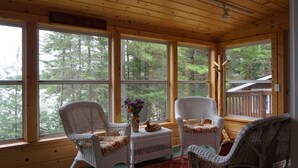 Una cabaña acogedora con ventanas amplias, muebles de mimbre y vistas al bosque.