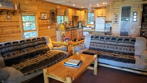 Un interior de cabaña con detalles de madera, un sofá, una mesa y una zona de cocina.