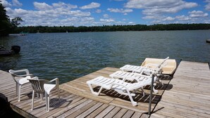 Un muelle de madera con sillones de jardín de plástico blanco y un pequeño bote.