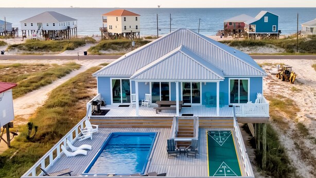 A beachfront house with a pool, deck chairs, and a shuffleboard table.