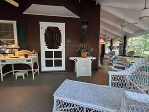 A covered outdoor seating area with wicker furniture, a white door, and a potted plant.