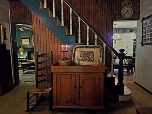 A staircase with wooden railings and a chandelier, leading to a dining area with a table and chairs. - ​Classic Victorian Gretna Cottage ▪︎ BYO Sheets & Towels (Mt Gretna)