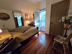 A bedroom with a bed, a chair, a desk, a window with curtains, a door, and a potted plant.