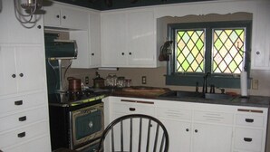 A compact kitchen with white cabinets, a vintage stove, and a window with a green frame. - ​Trailside Gretna Escape ▪︎ Walkable 3br Cottage  (Mt Gretna)