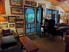 A cozy room with a wooden bench, a chair, a sofa, and a table. There are framed pictures on the wall and a window with a view.
