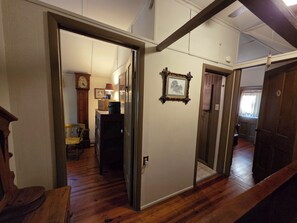 A hallway with wooden flooring, a framed picture on the wall, and a door leading to another room. - ​Classic Victorian Gretna Cottage ▪︎ BYO Sheets & Towels (Mt Gretna)