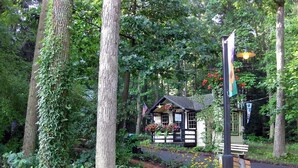 A rustic cabin surrounded by lush greenery, with a pathway leading to it. - ​Trailside Gretna Escape ▪︎ Walkable 3br Cottage  (Mt Gretna)