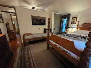 A bedroom with a wooden bed, a small sofa, a mirror, and a wall hanging. - ​Classic Victorian Gretna Cottage ▪︎ BYO Sheets & Towels (Mt Gretna)