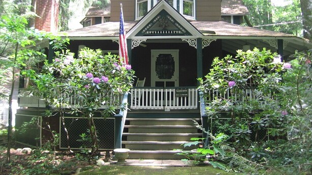 A two-story house with a porch, steps leading to the entrance, and an American flag. - ​Trailside Gretna Escape ▪︎ Walkable 3br Cottage  (Mt Gretna)