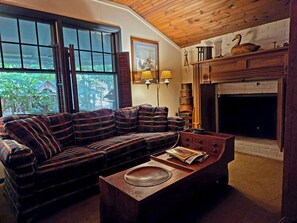 A cozy living room with a plaid sofa, a fireplace, and a window with curtains.