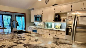 A modern kitchen with a granite countertop, stainless steel appliances, and white cabinetry. - Enjoy summer on the huge screen deck of this waterfront cabin! (Royal)