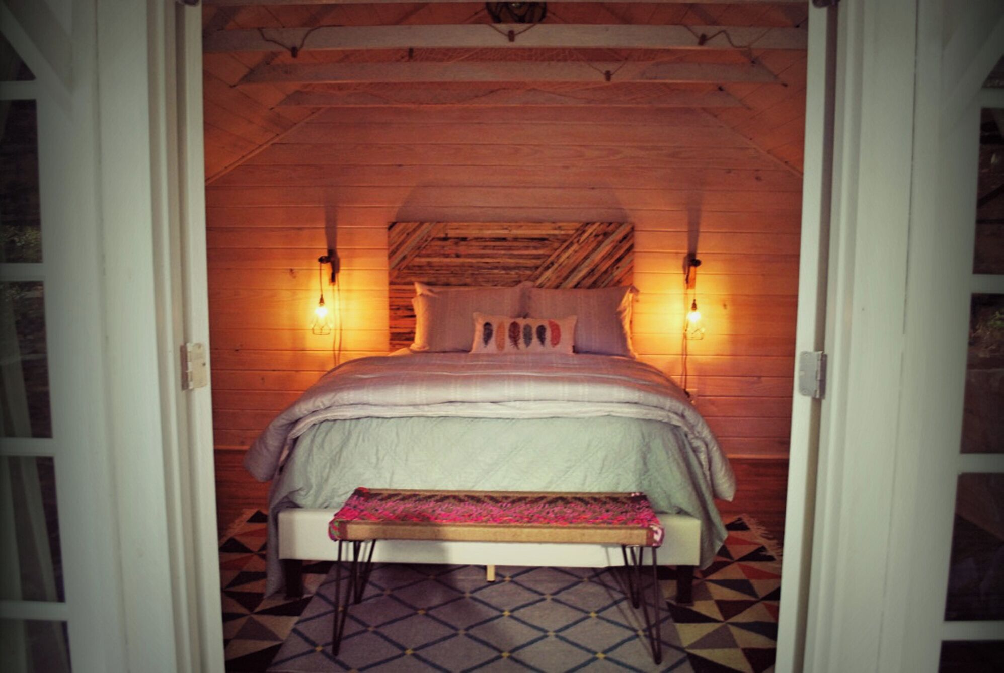A cozy bedroom with a bed, bedside lamps, and a patterned floor.