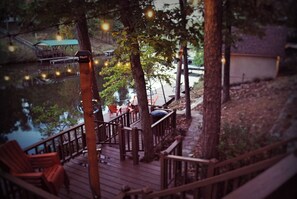Eine Holzterrasse mit Stühlen und Tischen, die auf ein Gewässer blickt, mit Lichterketten darüber.