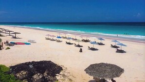 Ein Strand mit Liegestühlen und Sonnenschirmen, einem klaren Himmel und dem Meer.