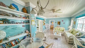 Ein Zimmer mit einem runden Glastisch, Korbstühlen, einer Couch und Regalen mit Dekoration.