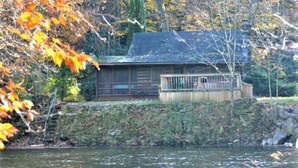 Una cabaña junto a un lago, con muelle de madera y un ventanal grande.